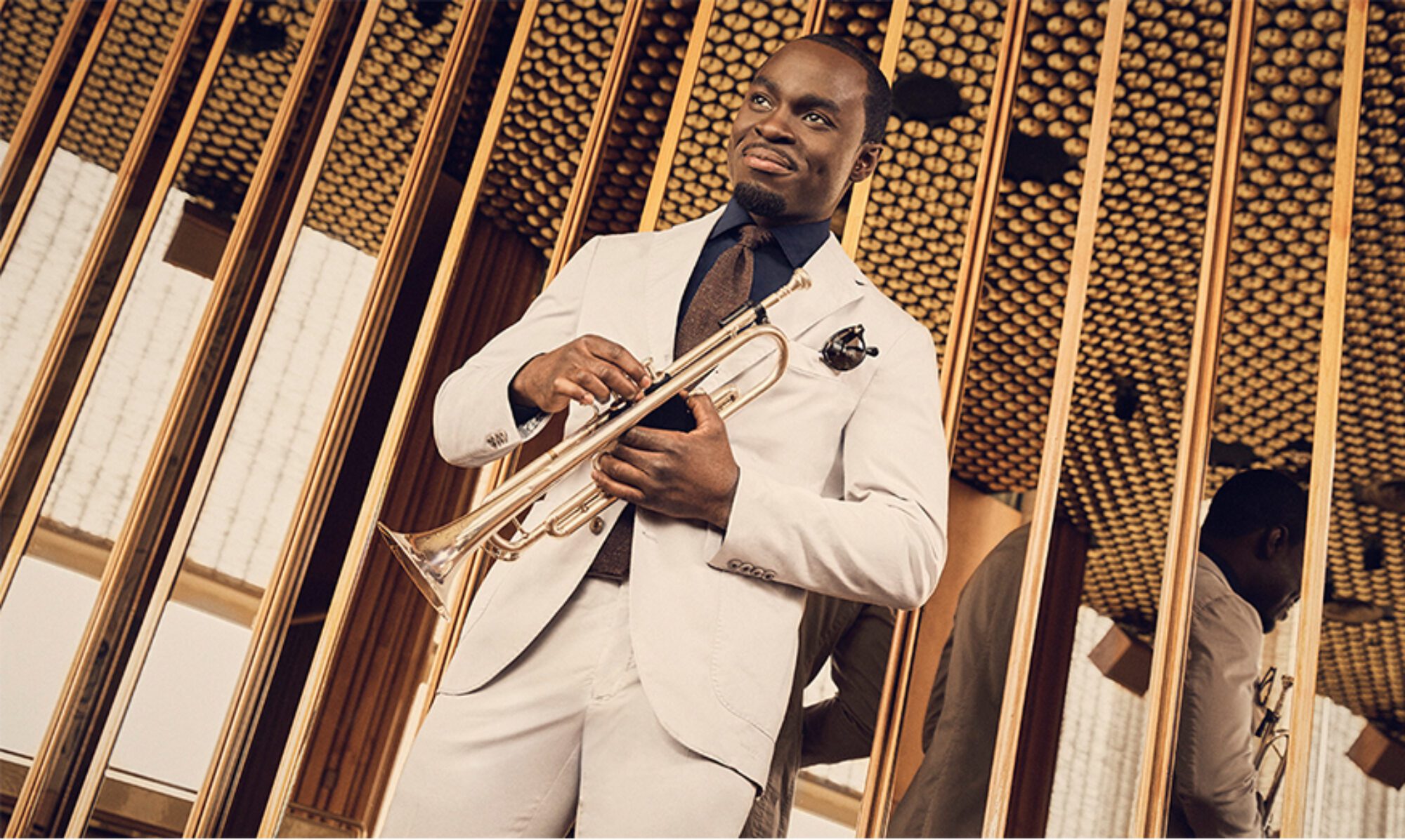 Man in white suit playing trumpet indoors with golden decor.
